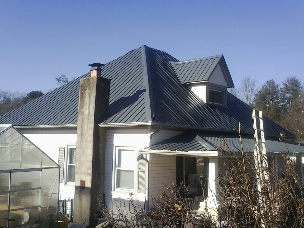 Dark blue standing seam metal roof on a white farmhouse with dormer — Slate & Tile Roof Repair by Roofing Brothers in South Otselic