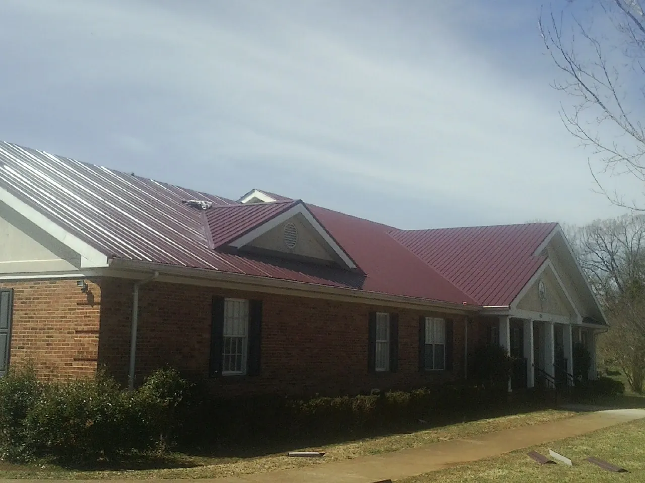 Red metal roof with gabled entries on a long brick building, from a Hail Damage Roof Repair job in South Otselic
