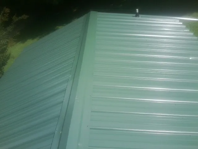 New green metal panels meeting at the ridge of a roof — Flat Roof Repair work by our crew in South Otselic
