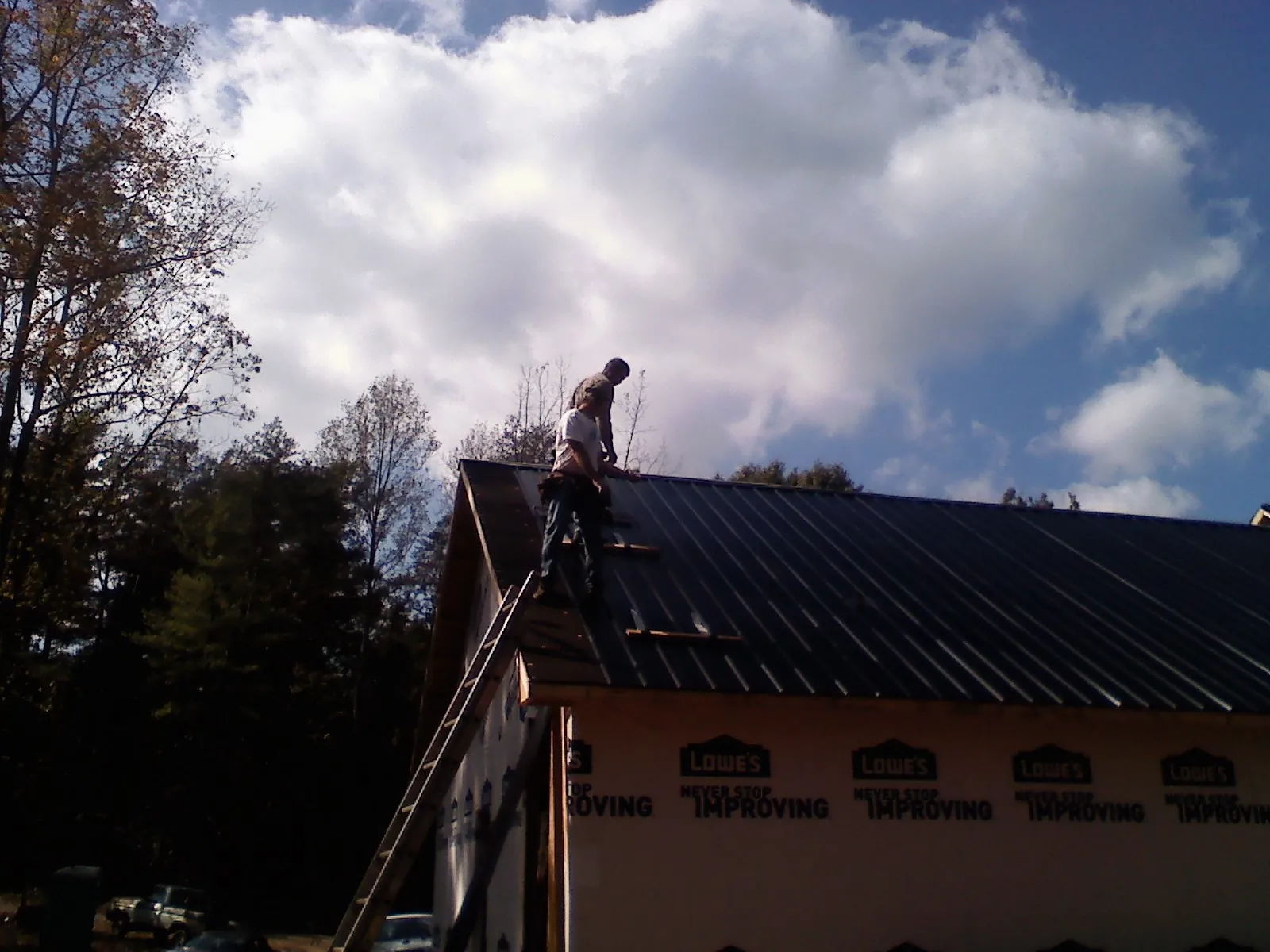 Roofer fastening dark metal panels high against a cloudy sky, from a Roof Inspection job in South Otselic