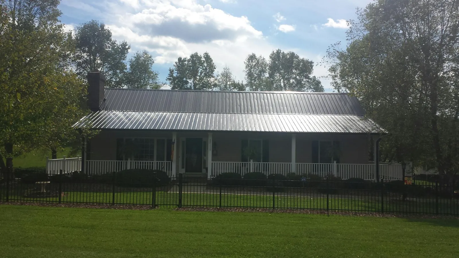 Gray metal roof on a brick ranch with a full width front porch — Gutter Guard Installation work by our crew in South Otselic