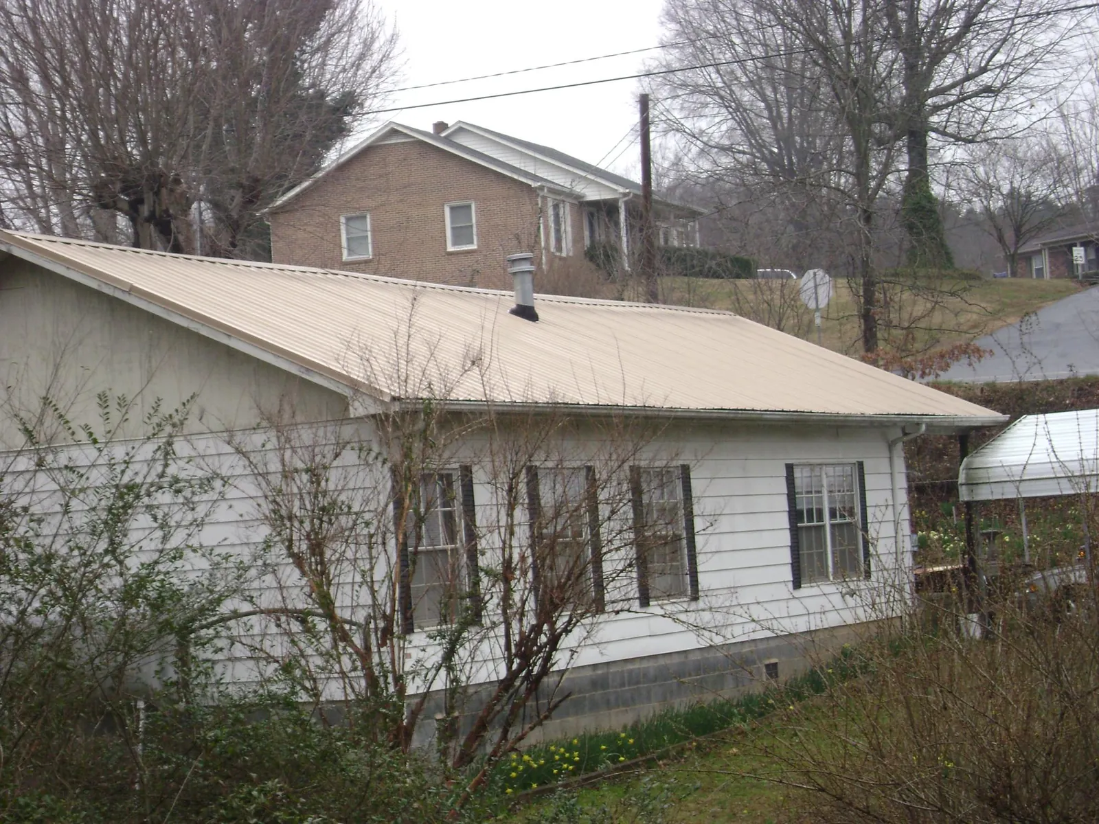 Tan metal roof on a white sided house set into a hillside — Commercial Roofing by Roofing Brothers in South Otselic