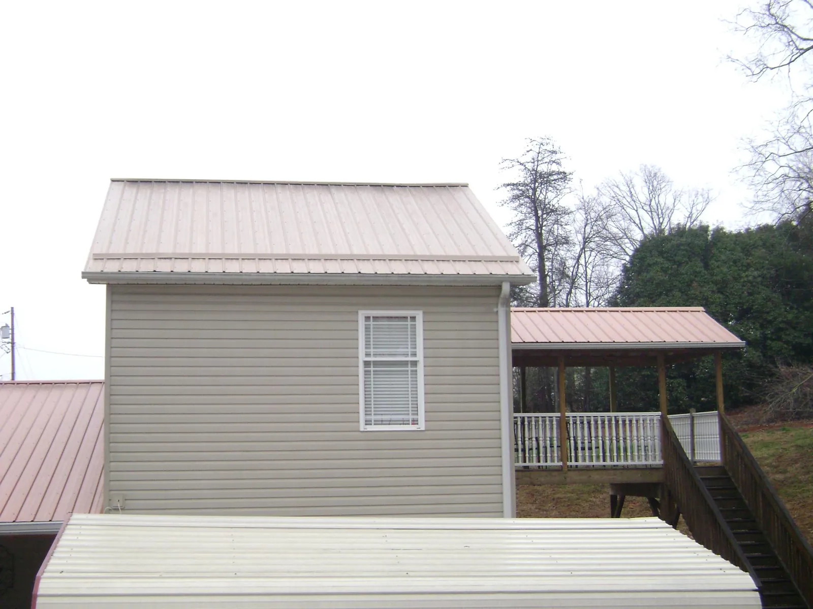 Tan metal roofs on a two story addition and attached porch, from a Roof Replacement job in South Otselic